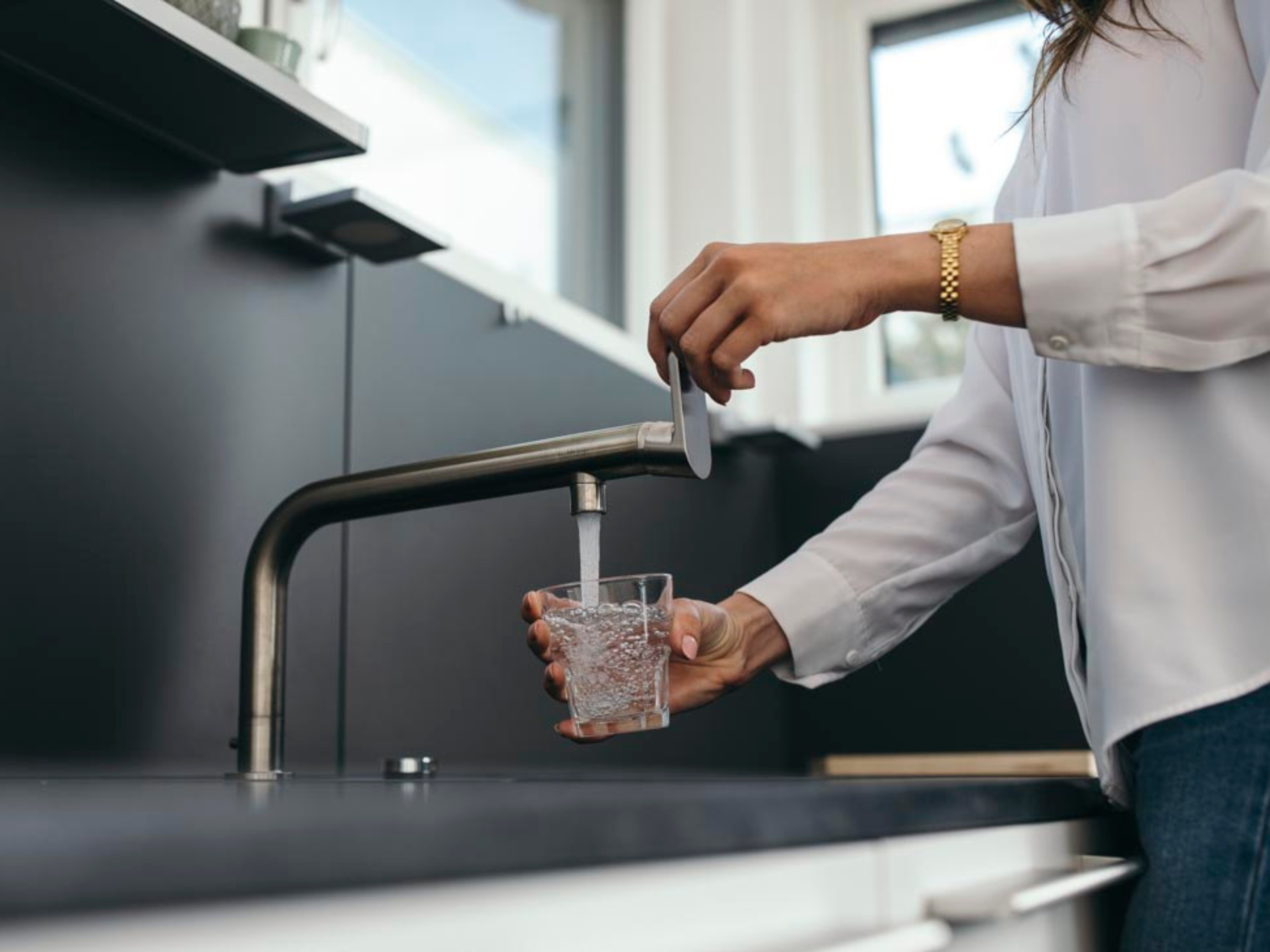 Frau schenkt sich ein Glas Wasser ein